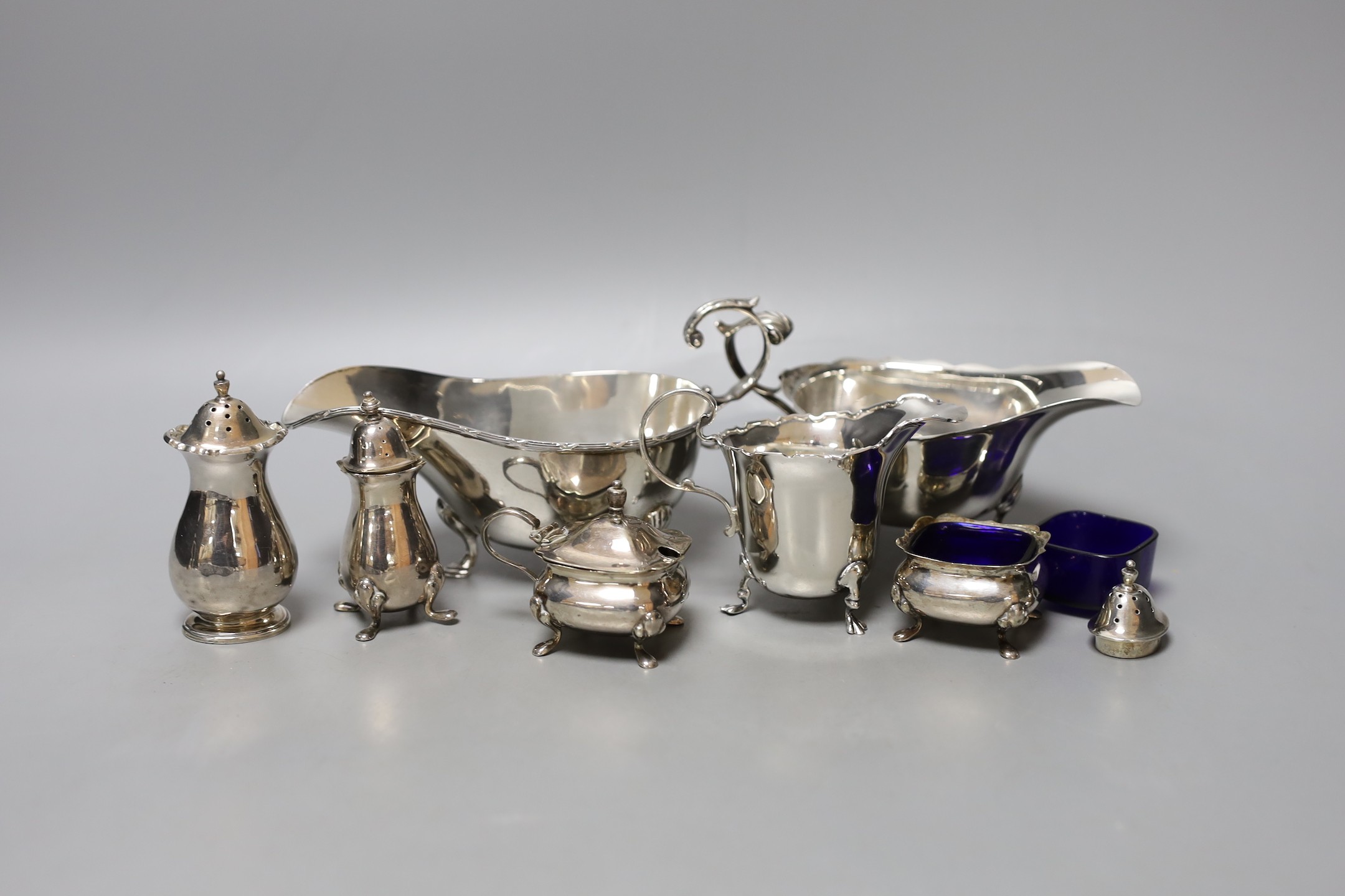 Two George V silver sauceboats, one a.f., a silver cream jug, four silver condiments, a lid and blue glass liner.